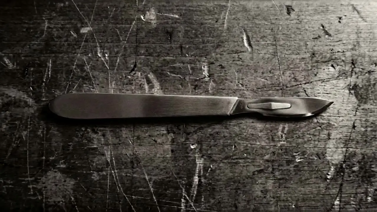 A surgical scalpel on a dark, marked work surface